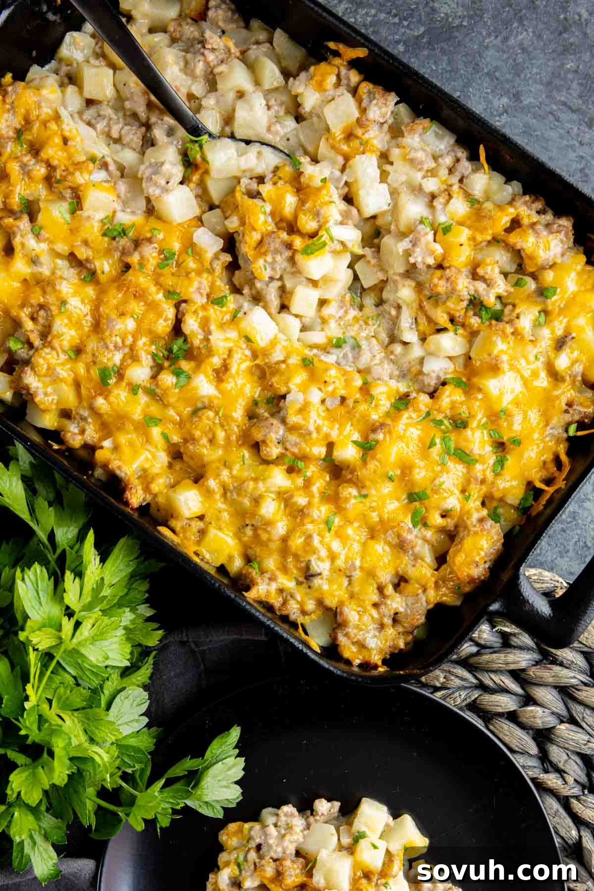 A close-up shot of the cheesy Sausage Potato Casserole in a rustic cast iron skillet, showcasing its golden crust and bubbly goodness.