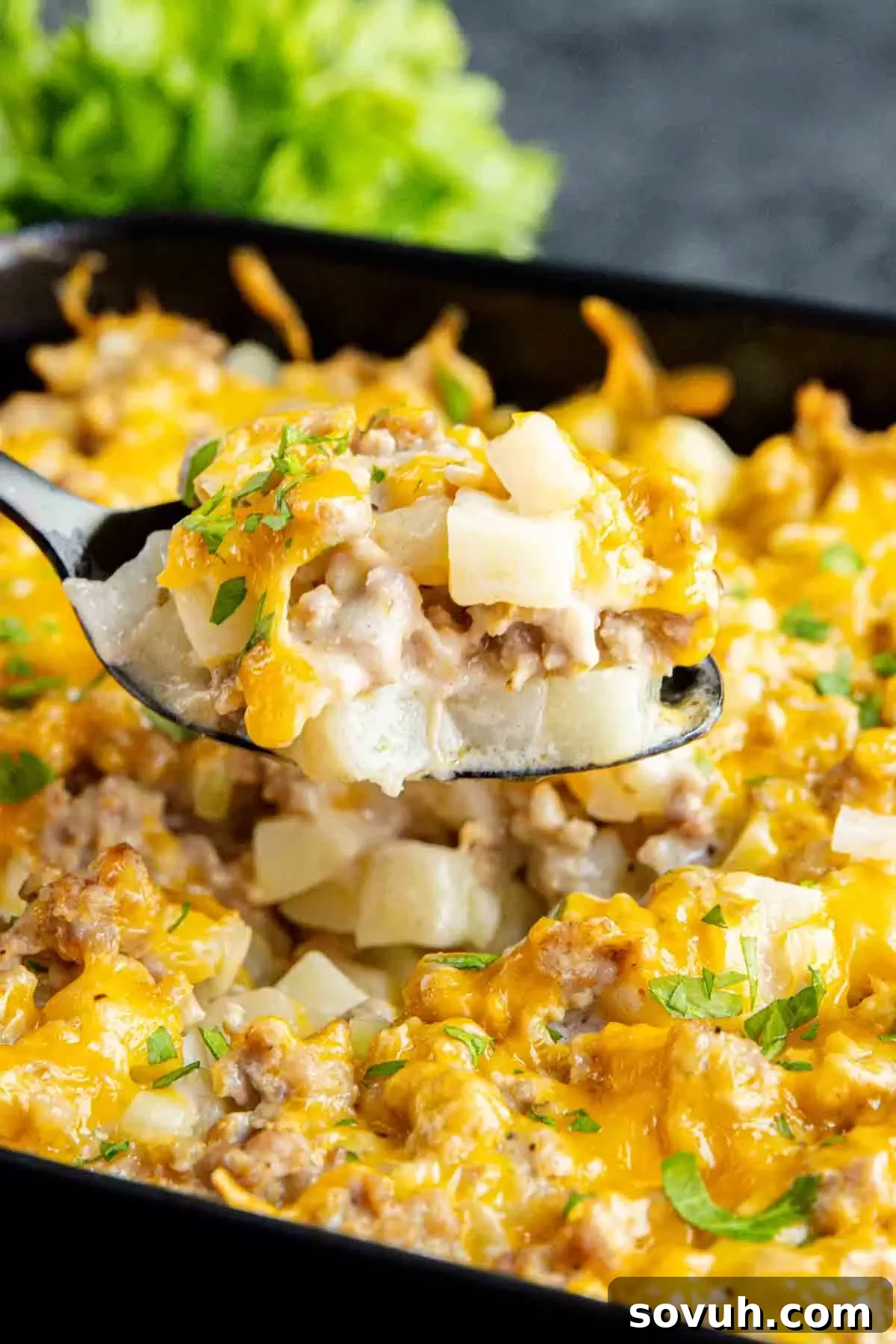 A spoonful of cheesy Sausage Potato Casserole being served from a skillet, highlighting its golden-brown top and creamy texture.