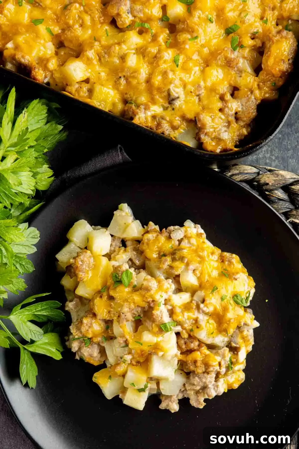 A perfectly portioned serving of cheesy Sausage Potato Casserole on a black plate, showcasing its golden cheese and hearty ingredients.