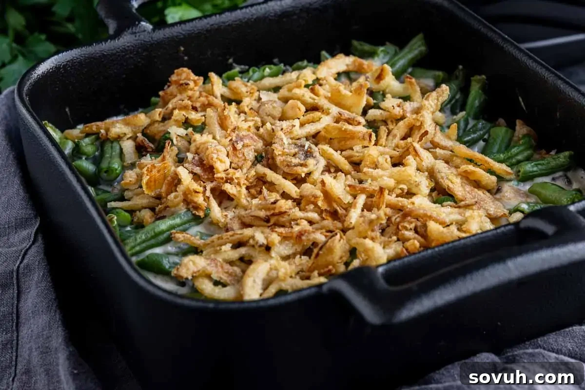 A black cast iron dish containing green bean casserole topped with crispy fried onions.