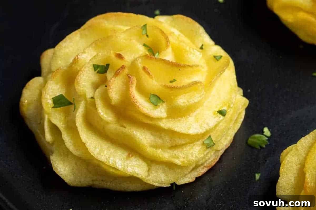 Close-up of a beautifully piped, golden-brown individual Duchess Potato swirl, delicately garnished with fresh parsley on a dark surface.