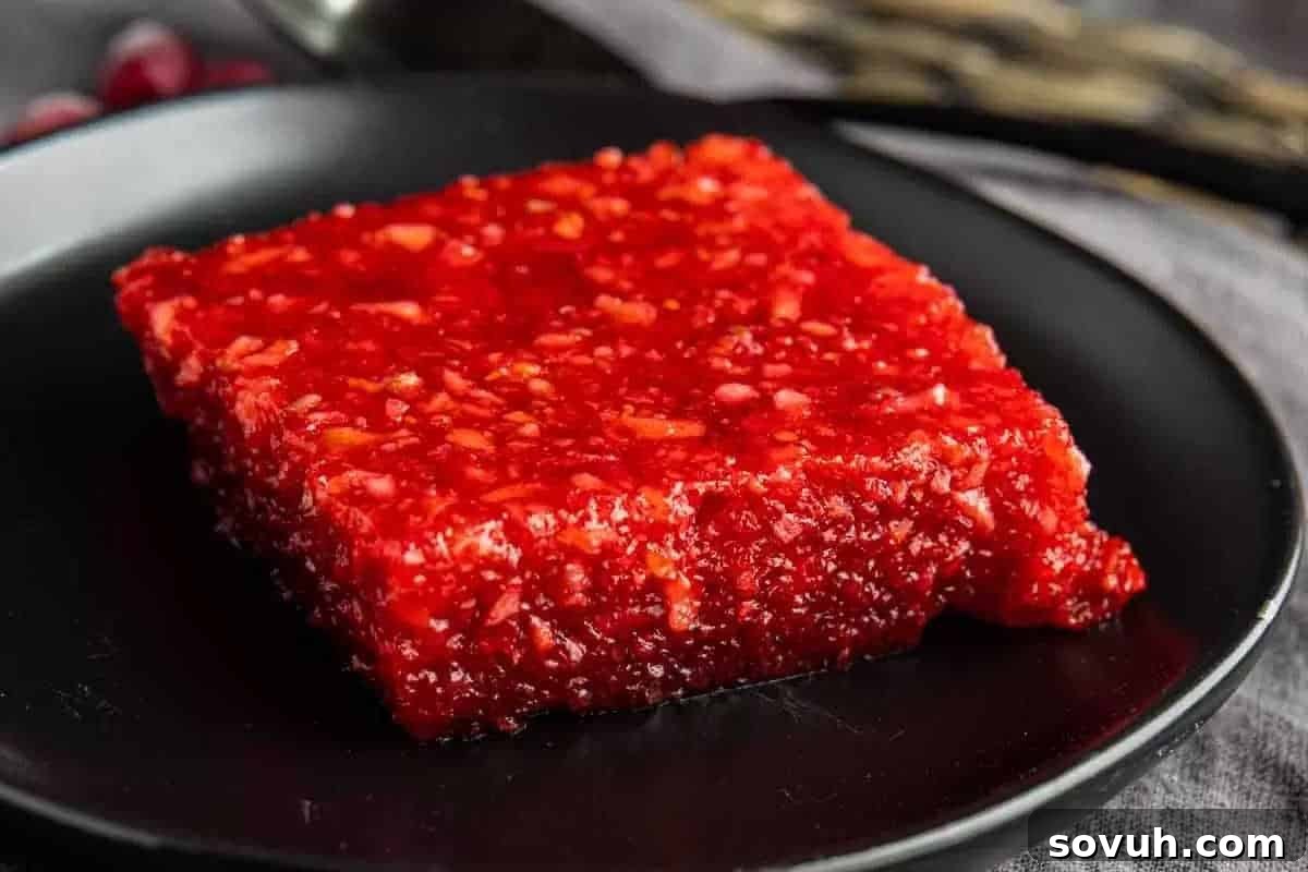 A glistening square of red Cranberry Jello Salad with visible fruit pieces, presented on a sleek black plate.