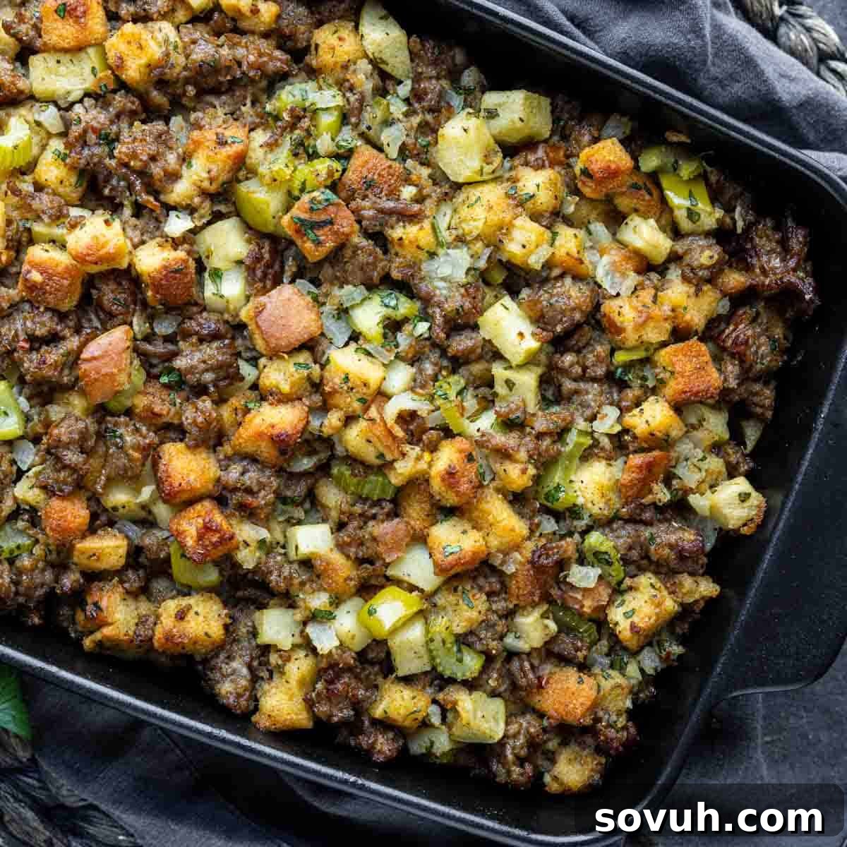 A baking dish filled with cooked stuffing, featuring bread cubes, sausage, diced celery, onions, and herbs.
