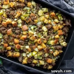 A baking dish filled with cooked stuffing, featuring bread cubes, sausage, diced celery, onions, and herbs.