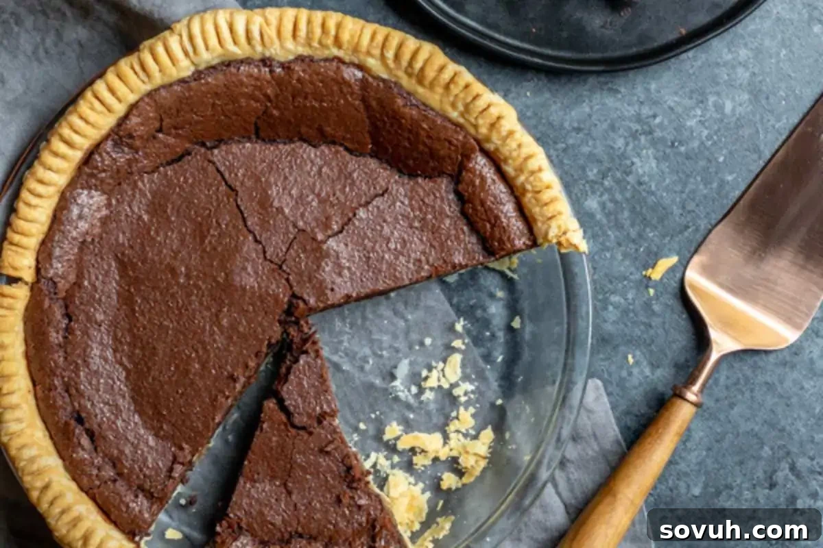 A chocolate pie in a glass dish with two slices cut out, resting on a gray surface, is one of those irresistible desserts. A metal serving spatula with a wooden handle lies beside the dish, ready for you to gobble 'til you wobble.