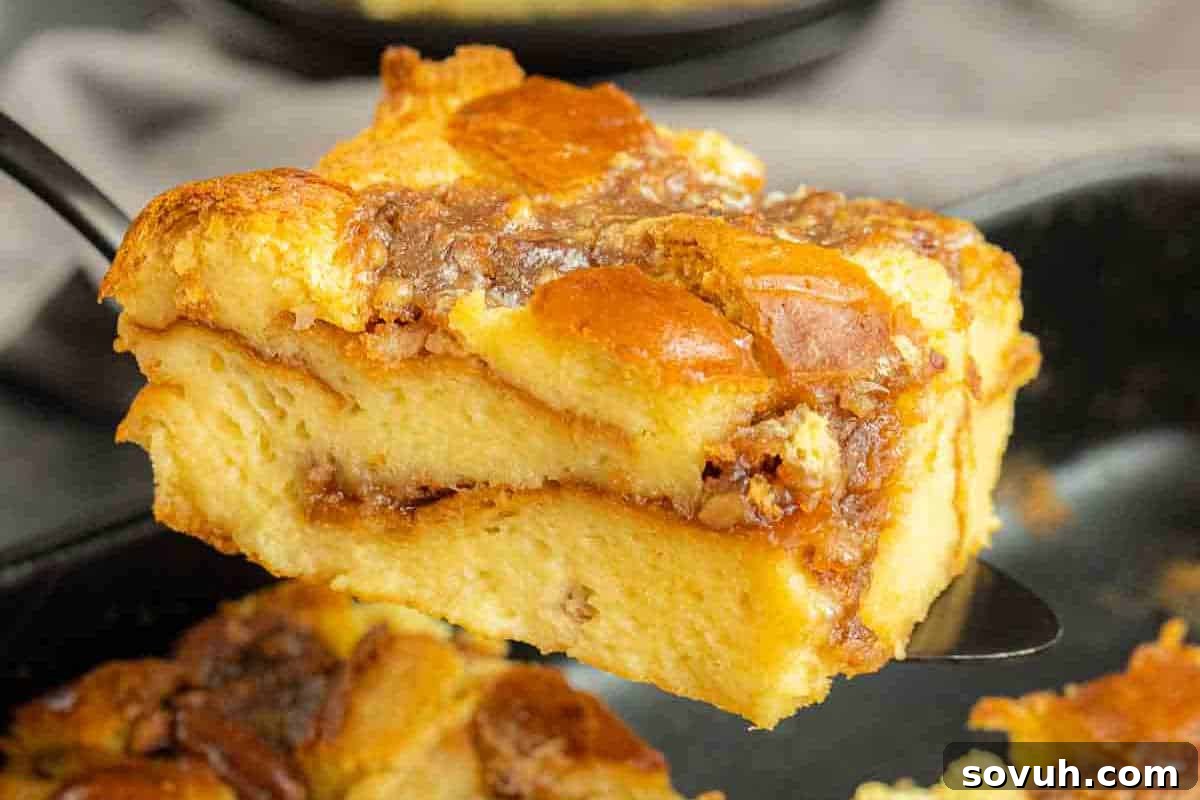 A slice of bread pudding with a golden-brown top, held on a spatula over a baking dish.