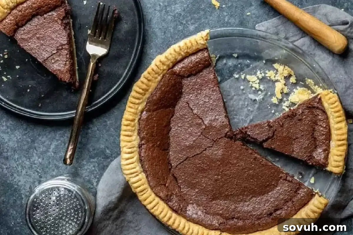 A chocolate pie in a glass dish with two slices removed; one slice is on a black plate with a fork. A knife and shaker are nearby on a dark surface.