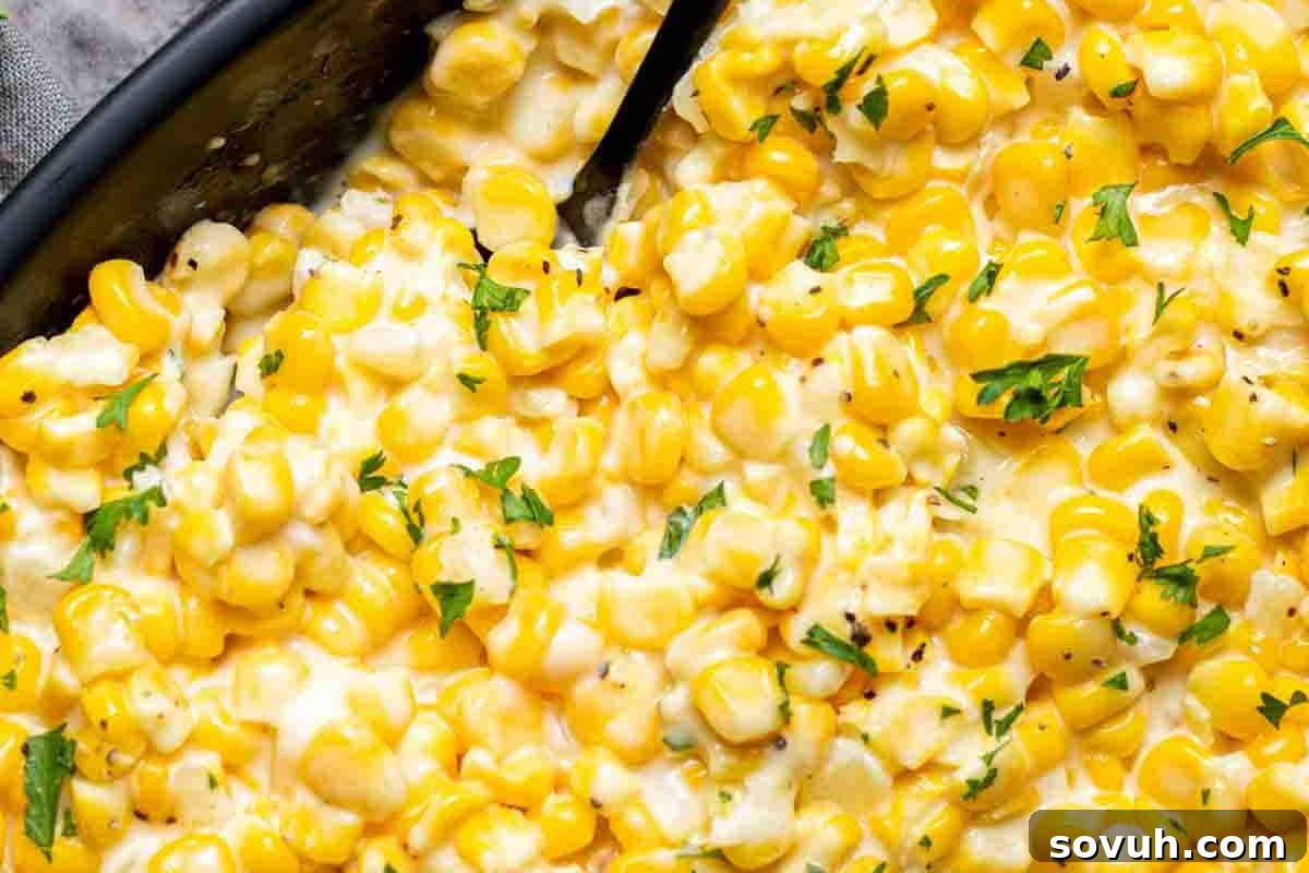 Close-up of creamy corn dish topped with chopped parsley, served in a black dish.