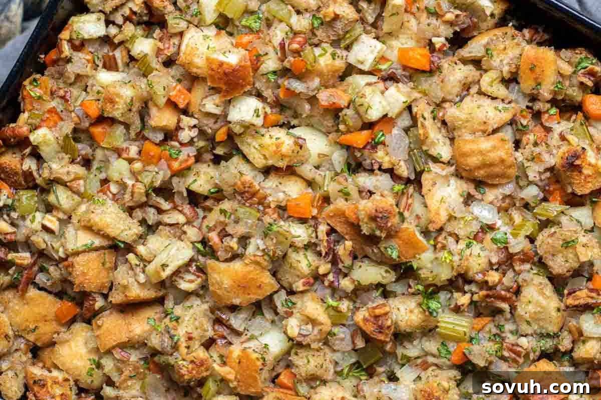 A close-up view of a golden-baked dish of Apple Pecan Stuffing, highlighting fluffy bread cubes, tender diced carrots, crisp celery, savory onions, and fragrant herbs, creating a rich and inviting texture.
