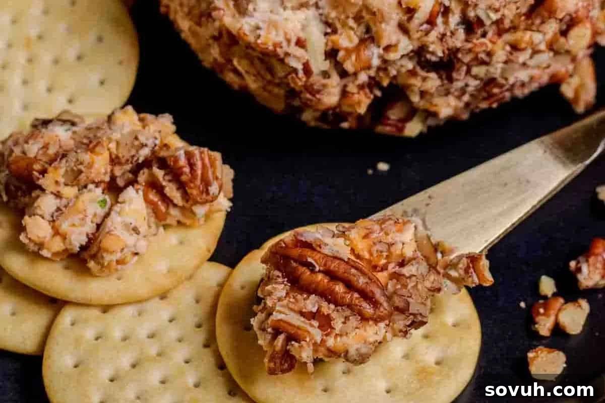 Crackers topped with a spread made of cheese and pecans on a dark surface. A knife with the spread is also visible.