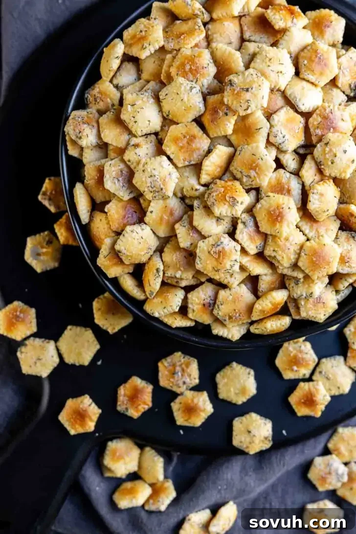A bowl filled with hexagonal seasoned crackers, with some scattered on a dark surface.