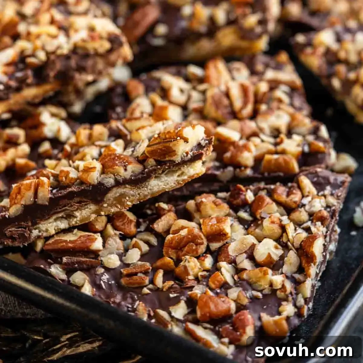 Close-up of toffee topped with melted chocolate and chopped pecans on a baking tray.