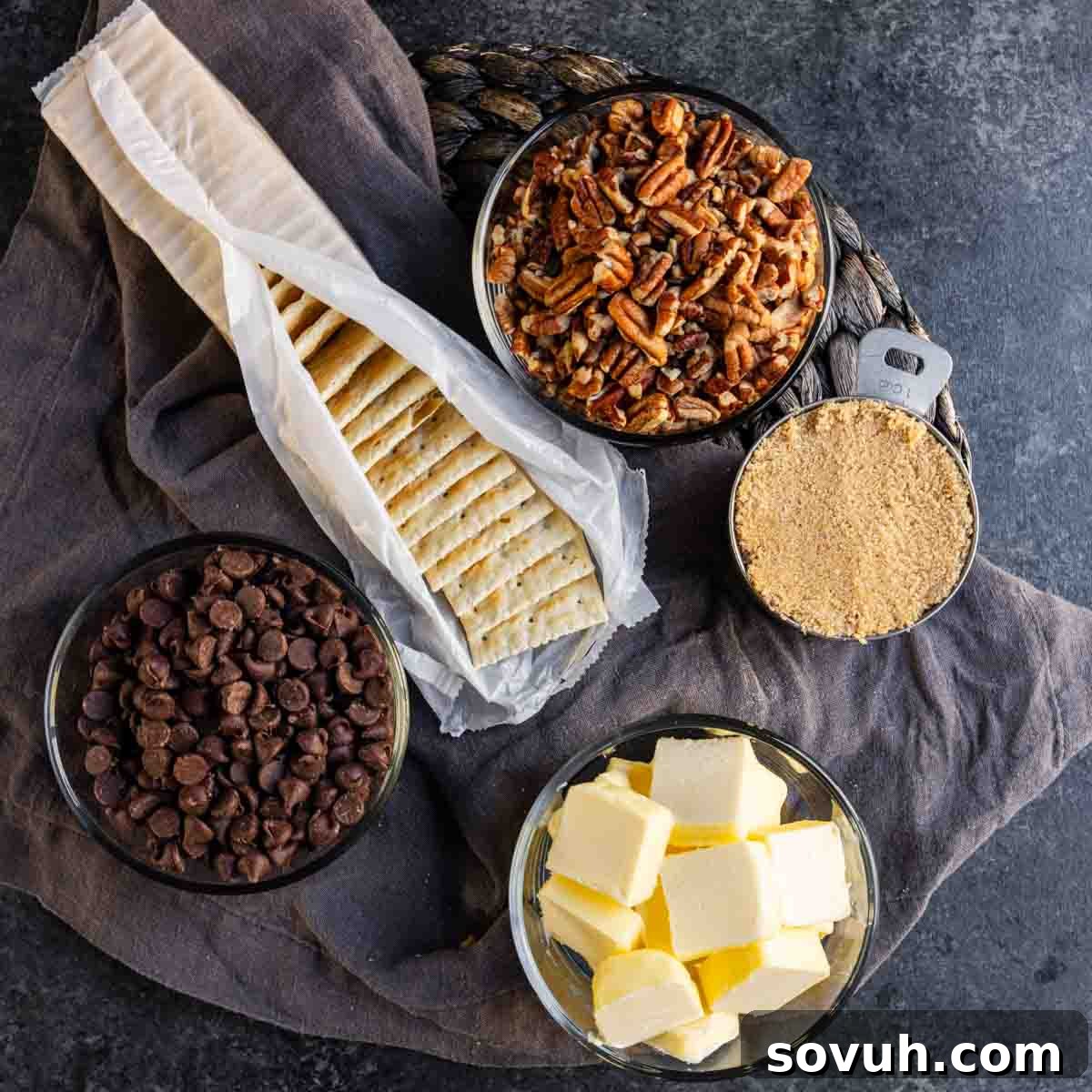 Ingredients on a dark surface: graham crackers, pecans, brown sugar, chocolate chips, and cubed butter.