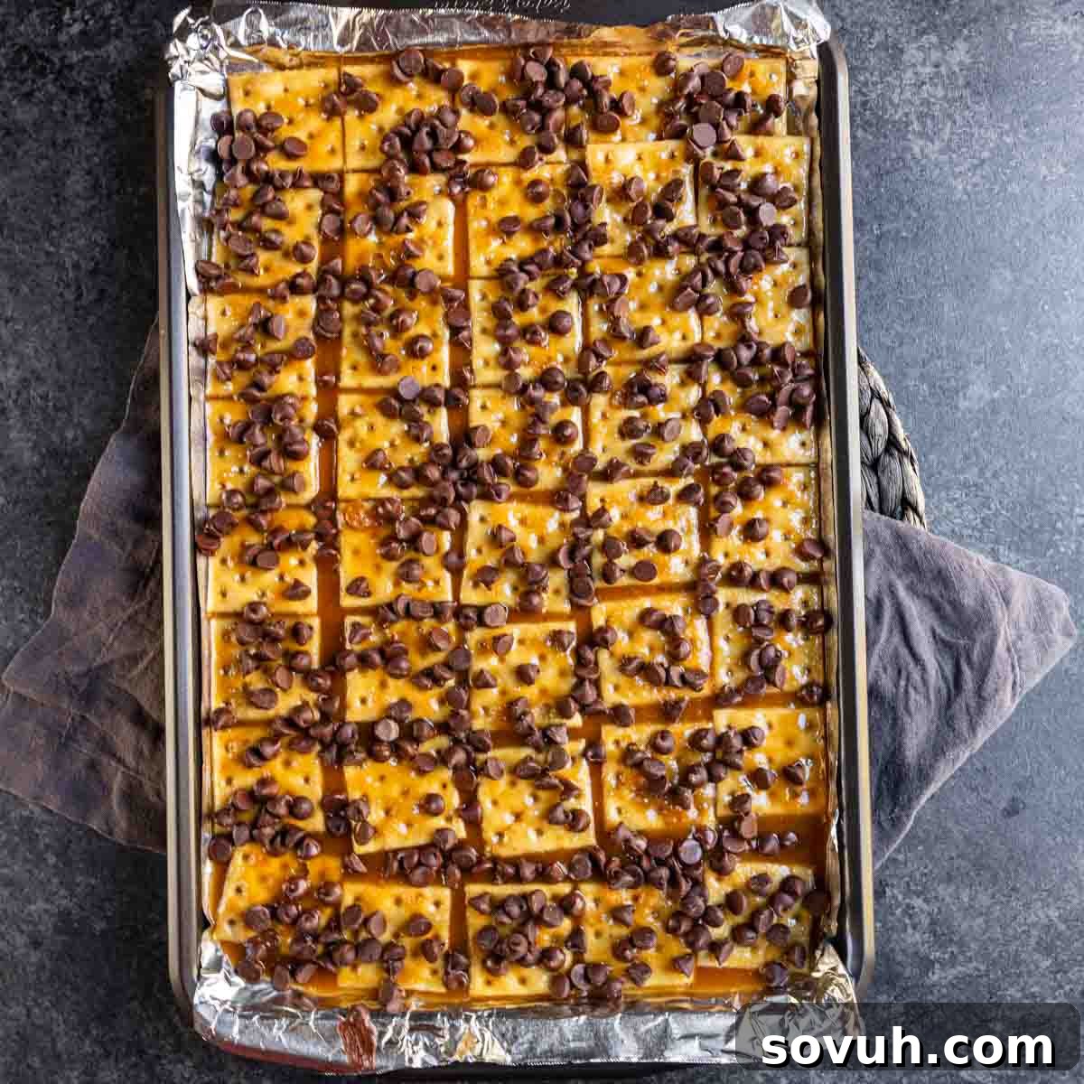 Baking tray with chocolate chip and caramel cracker squares on foil.