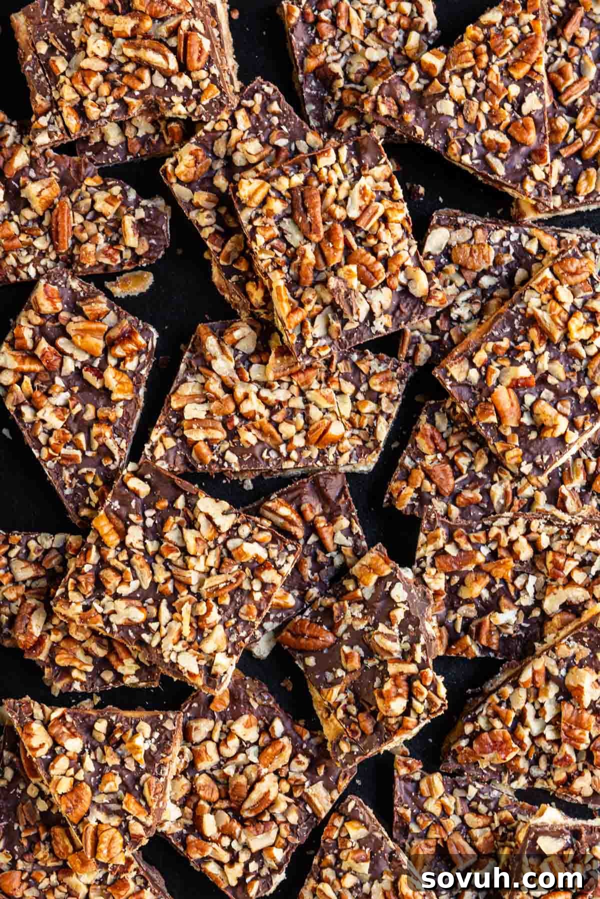 Squares of chocolate toffee brittle topped with chopped pecans, overlapping each other.