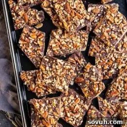 Pieces of chocolate bark topped with chopped pecans on a baking tray.