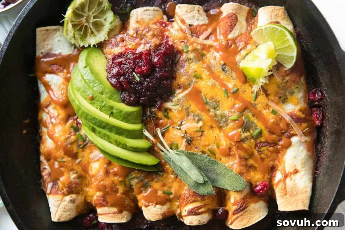 A vibrant skillet of baked Thanksgiving Leftover Enchiladas, richly topped with melted cheese, fresh sliced avocado, a dollop of cranberry sauce, and bright lime wedges, garnished with fresh herbs.