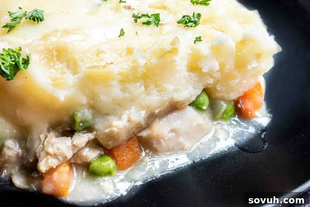 Close-up of a generous slice of creamy Turkey Shepherd's Pie with a rich mashed potato topping, visible chunks of turkey, tender green peas, and vibrant carrots, garnished with fresh parsley on a black plate.