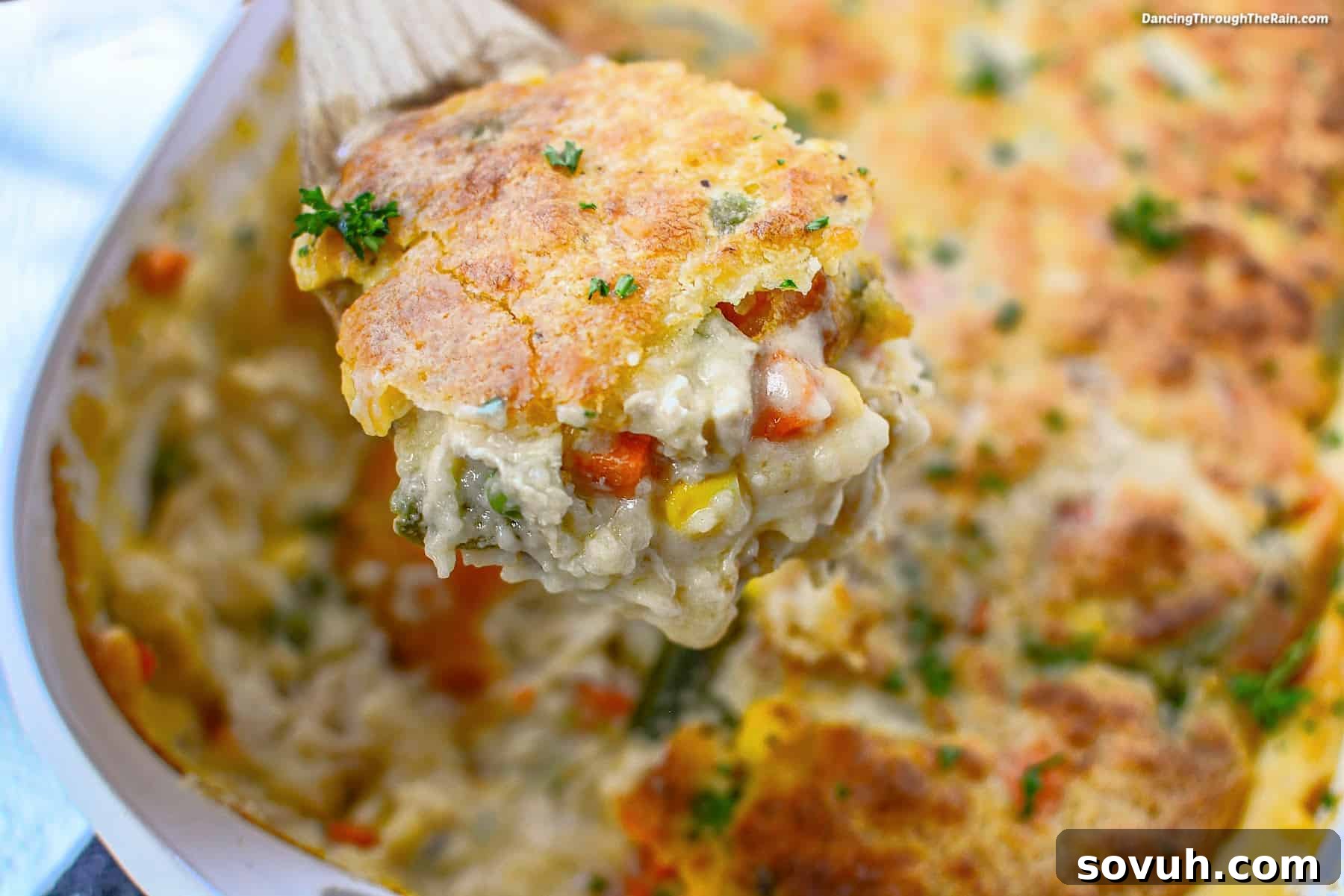 Close-up of a vibrant and comforting turkey pot pie, showcasing a golden-brown, flaky Cheddar Bay Biscuit crust being scooped, revealing a rich filling of mixed vegetables and creamy turkey inside.