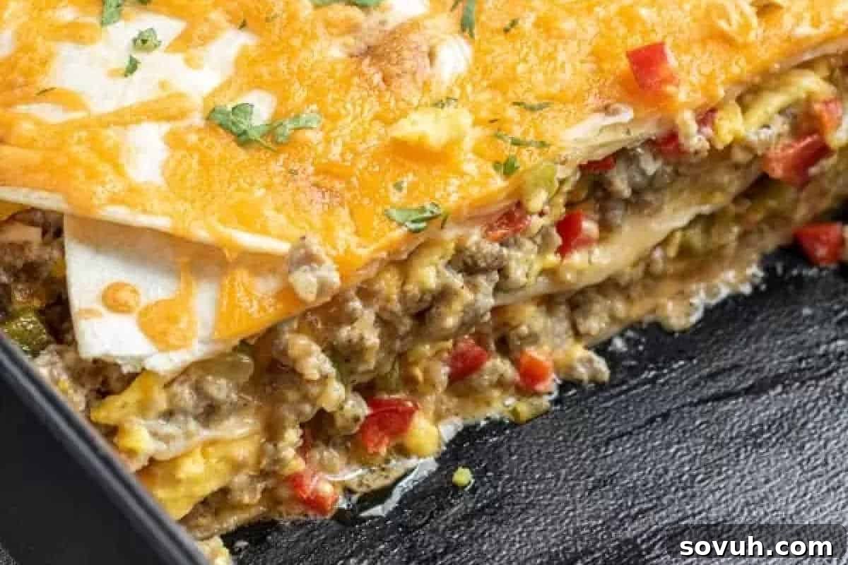A close-up of a cheesy Breakfast Burrito Casserole with layers of ground meat, tortillas, and vegetables, partially cut to show the inside.