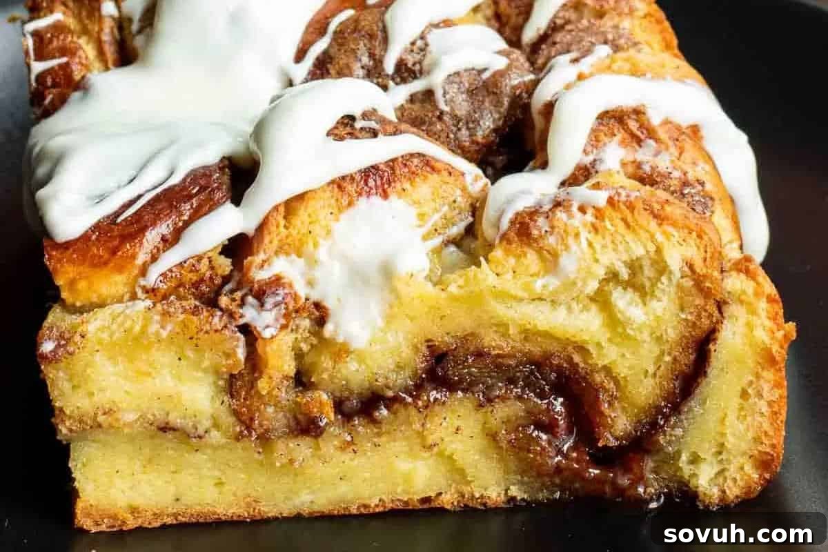 Close-up of a cinnamon roll with swirls of cinnamon and white icing on top, set on a dark background, representing a delicious French toast casserole.