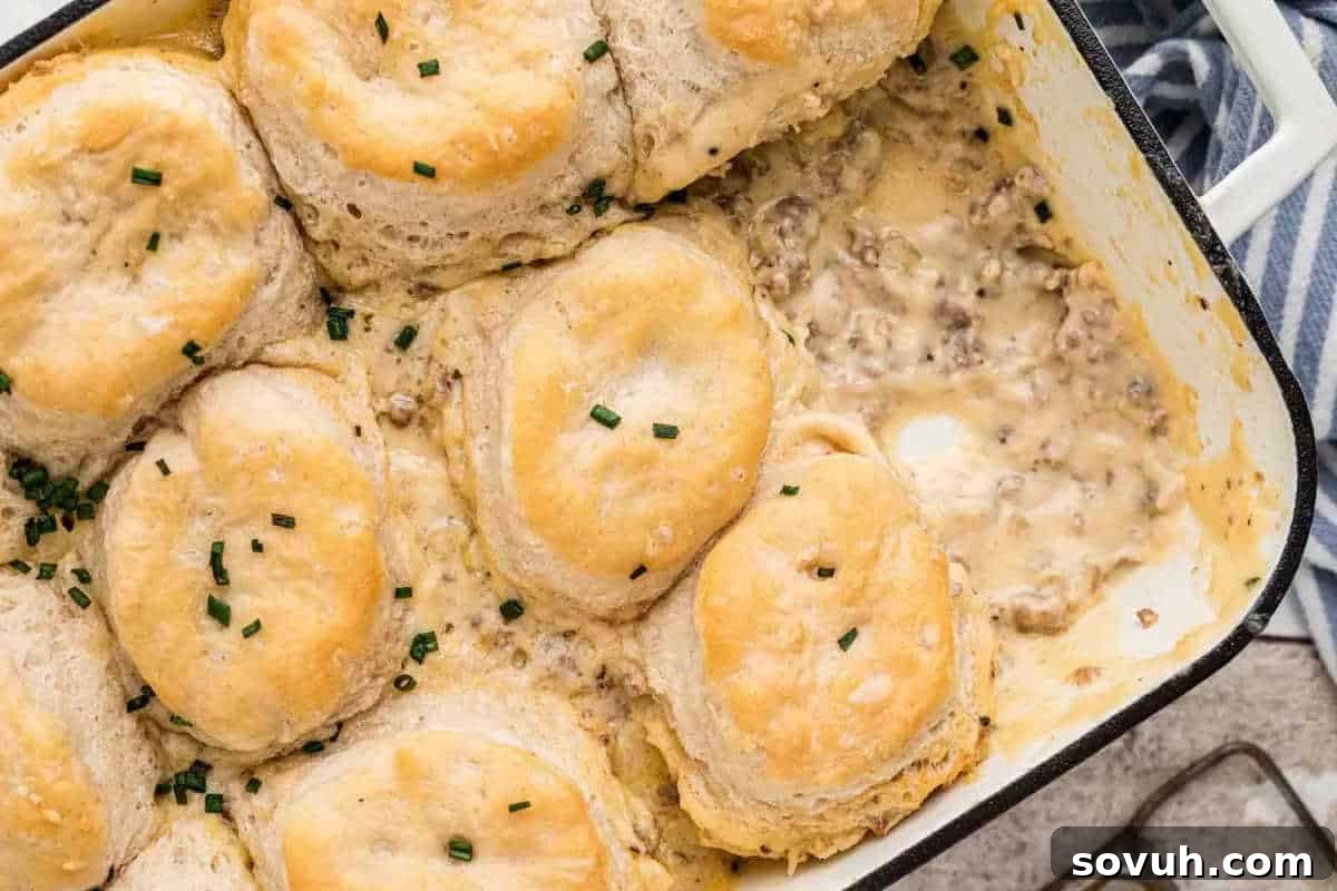 Baked breakfast casserole with fluffy biscuits on top of creamy, seasoned ground meat mixture, garnished with chopped chives, a comforting breakfast idea.