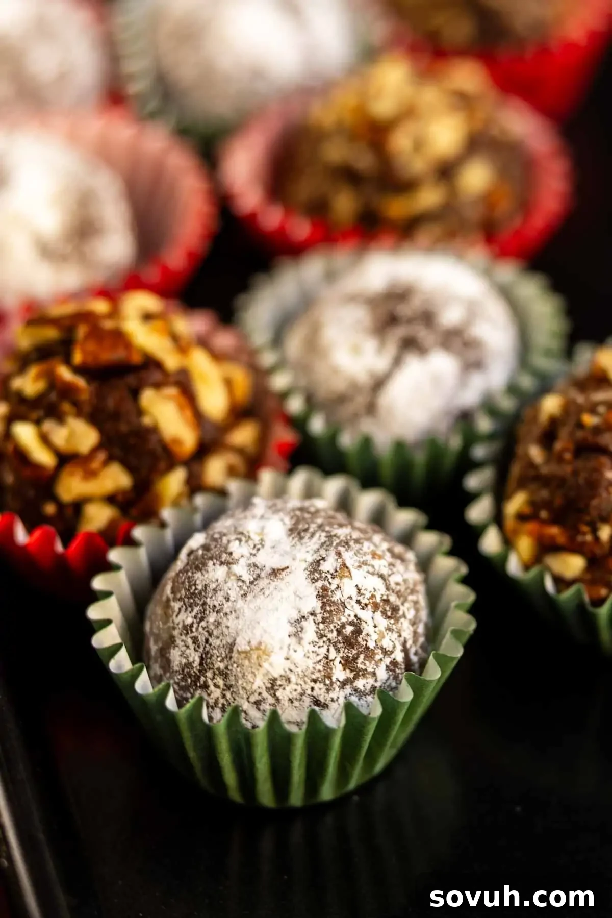 Chocolate truffles dusted with powdered sugar in colorful paper cups, some topped with chopped nuts.