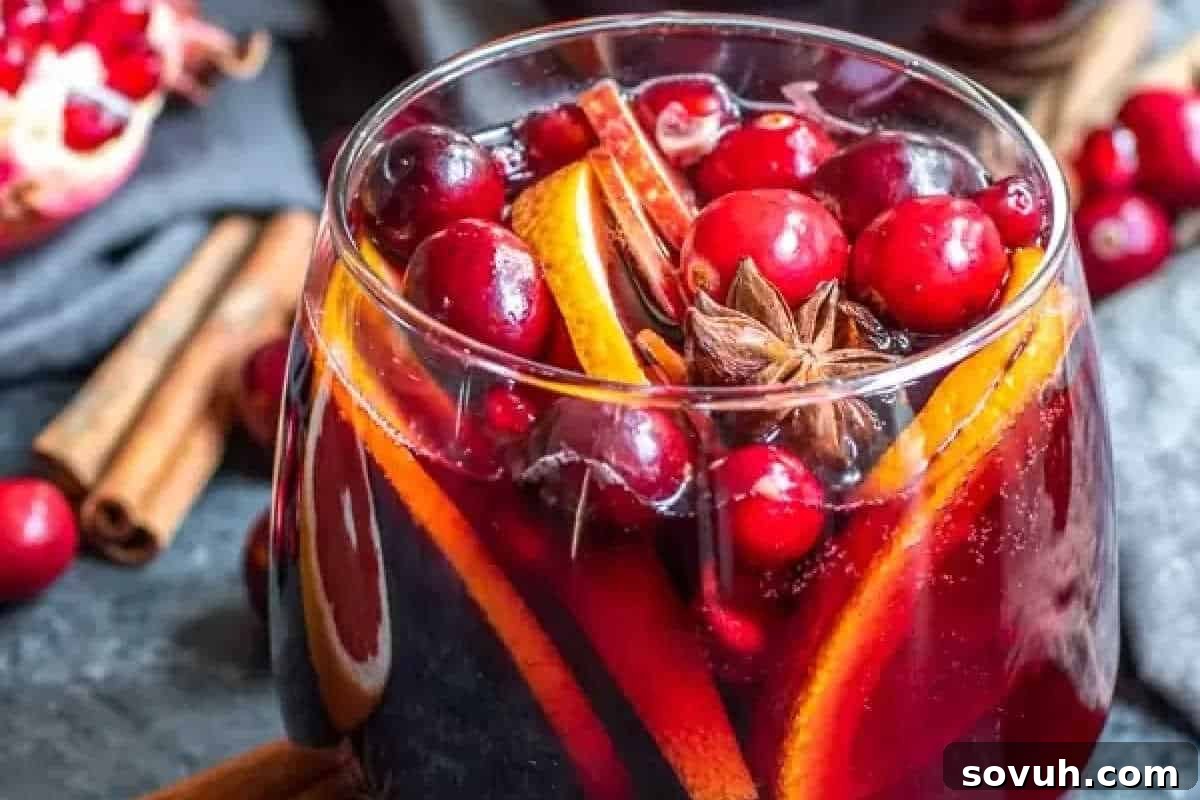 A festive glass of rich red mulled wine, garnished with vibrant orange slices, ruby red cranberries, and exotic star anise, surrounded by fragrant cinnamon sticks and scattered pomegranate seeds, creating a cozy holiday ambiance.