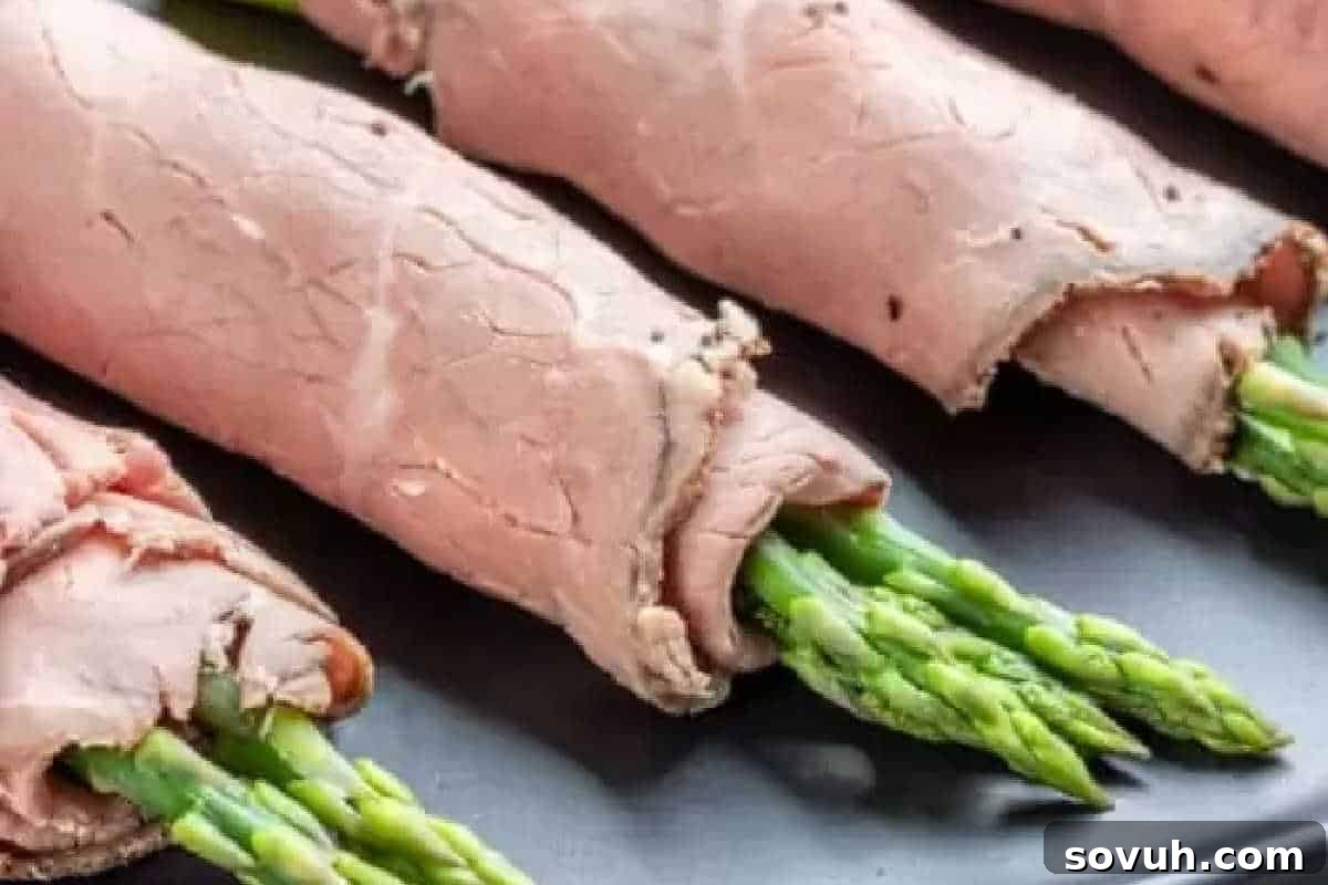 Elegant slices of tender roast beef meticulously wrapped around crisp, vibrant asparagus spears, artfully arranged on a dark, sophisticated surface, presenting a healthy and flavorful appetizer.
