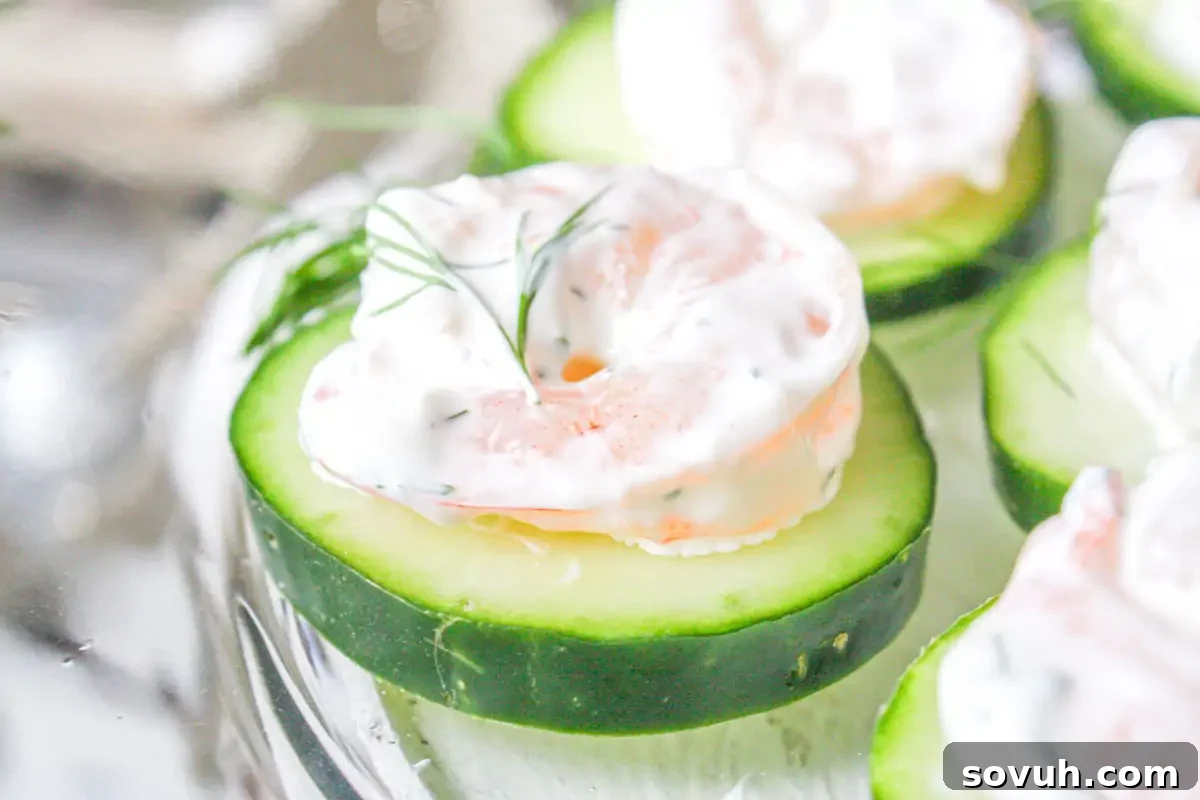 Refreshing cucumber slices elegantly topped with succulent shrimp and a delicate dollop of dill cream, artfully arranged on a pristine white platter, creating a light and flavorful appetizer.