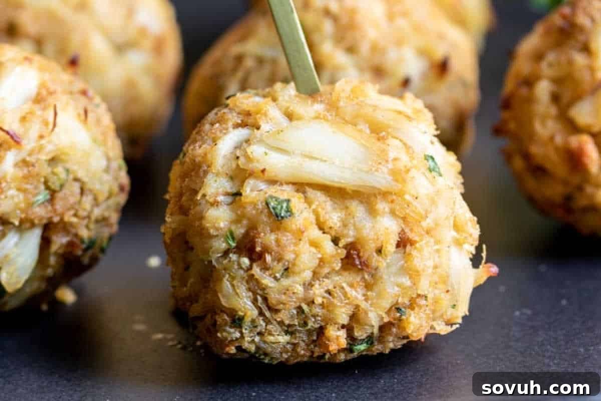 A perfectly golden-brown crab cake, impaled with a toothpick for easy serving, highlighting its seasoned breadcrumb crust and hints of fresh herbs, presented against a dark, elegant background.