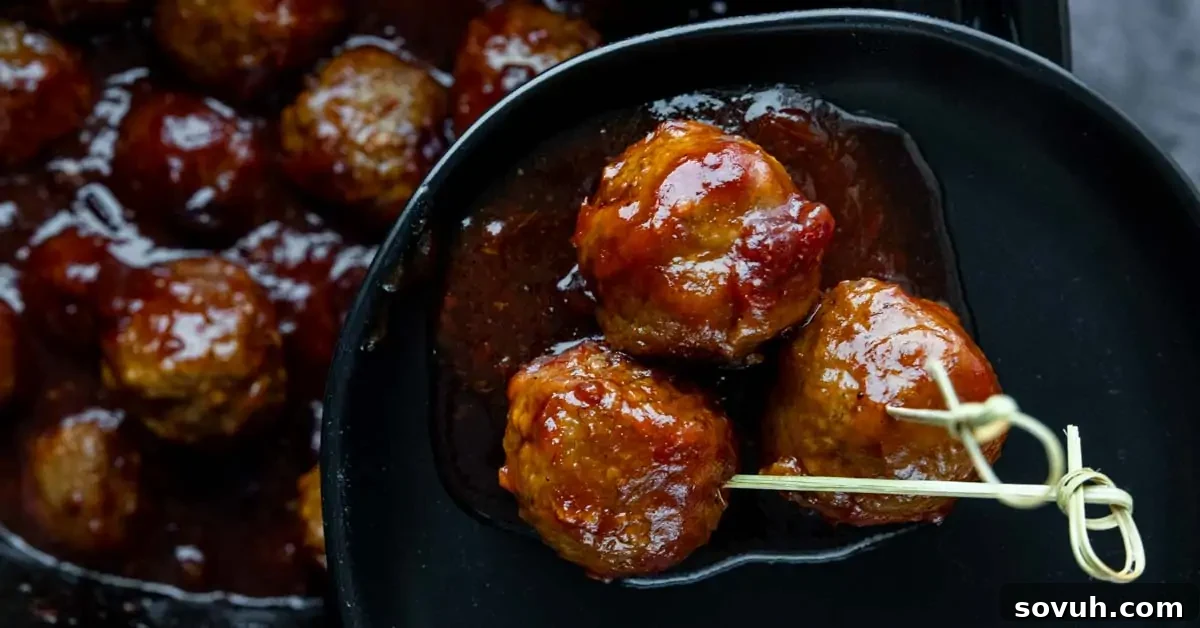 Three perfectly glazed meatballs artfully arranged on a black plate, with one pierced by a toothpick, showcasing their succulent texture and sticky cranberry sauce coating, with more meatballs blurred in the background.