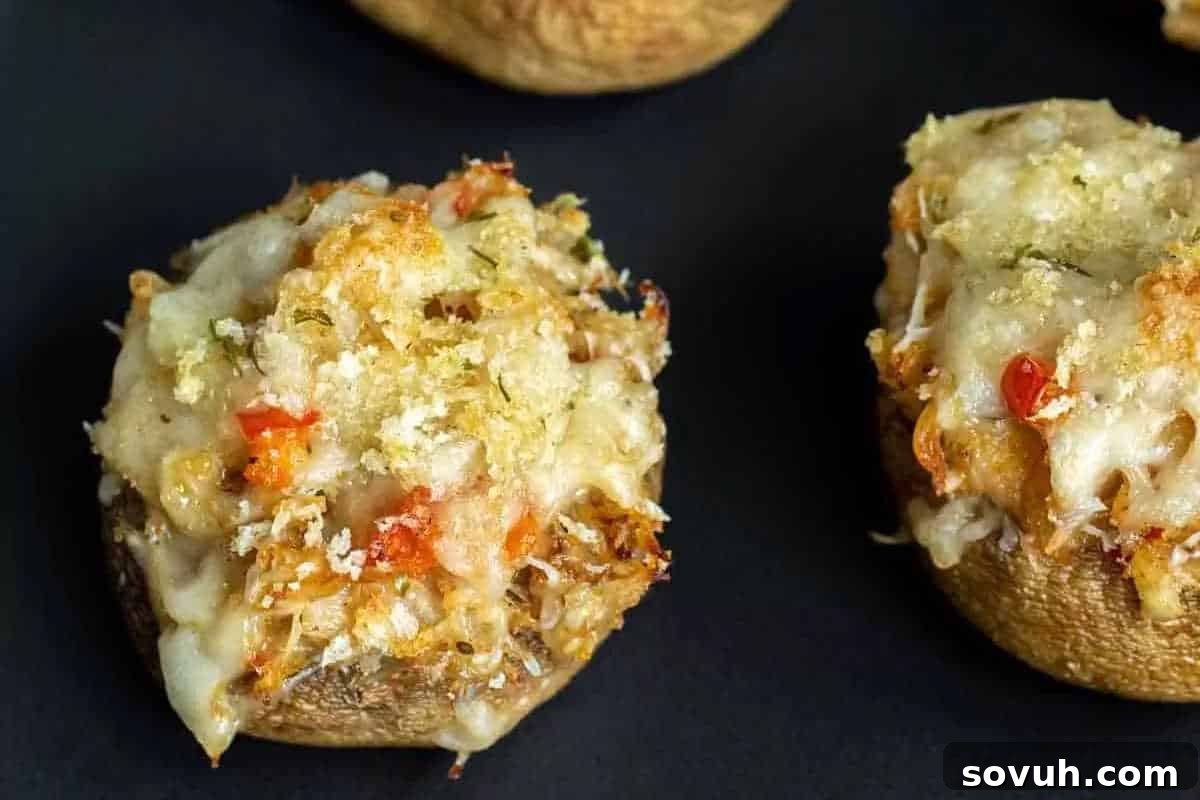 An enticing close-up of tender stuffed mushrooms, generously topped with melted, bubbly cheese and fragrant fresh herbs, perfectly baked and presented on a dark, elegant surface.