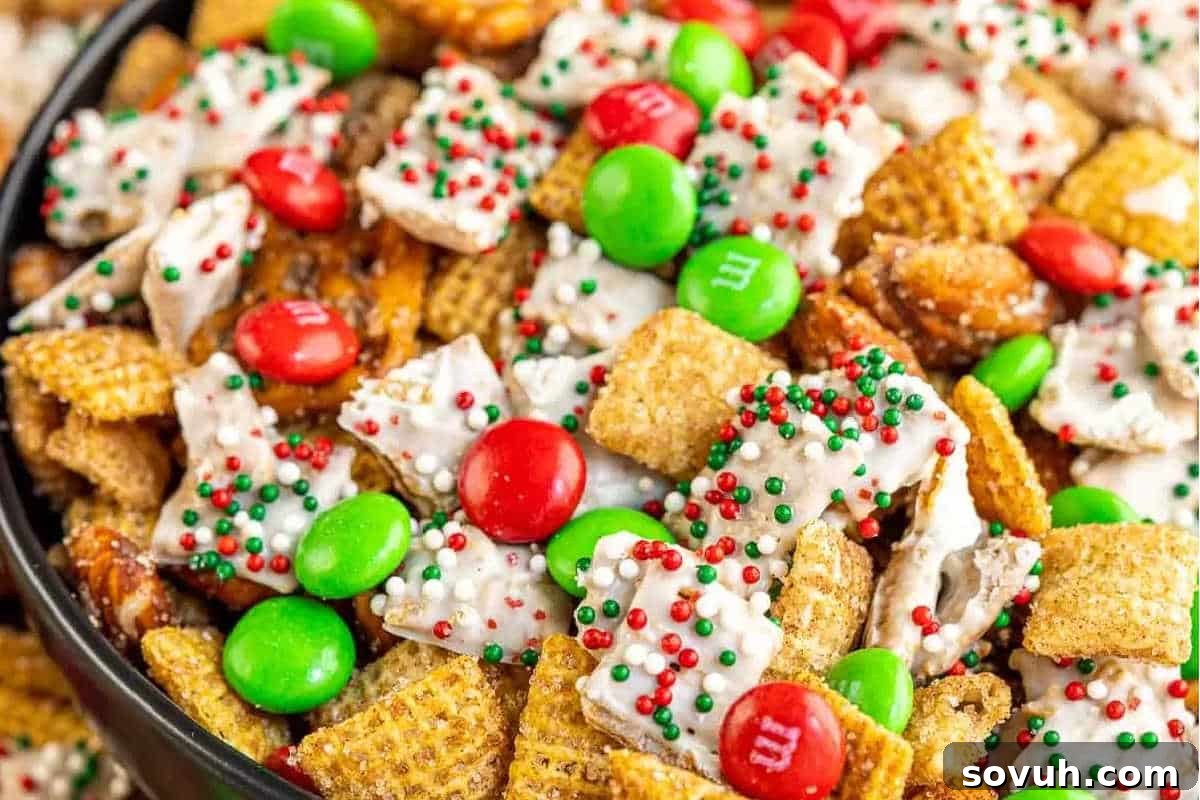 A vibrant close-up of Christmas Chex Mix, featuring cereal pieces generously coated in a shimmering white glaze, interspersed with festive red and green candies and playful holiday sprinkles.