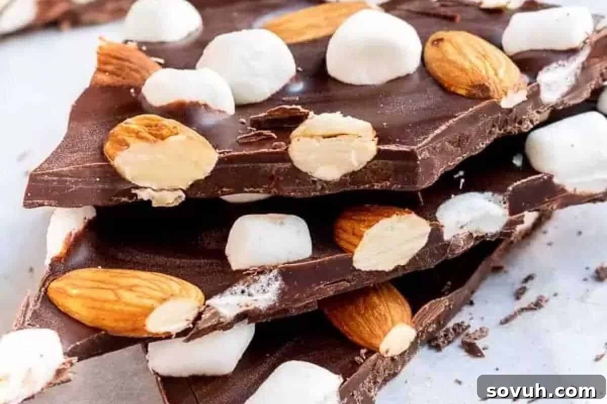 A delectable stack of Rocky Road Chocolate Bark pieces, richly studded with fluffy marshmallows and crunchy almonds, creating an inviting texture against a clean white background.
