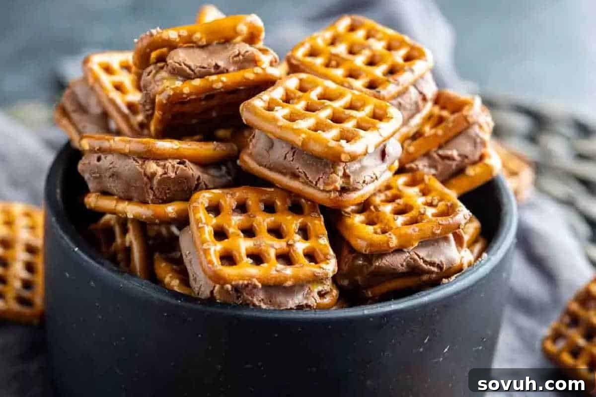A sleek black bowl brimming with an enticing array of Snickers Pretzel Bites, featuring melted Snickers bars nestled between two crispy pretzel squares, forming irresistible chocolate-covered pretzel sandwiches.