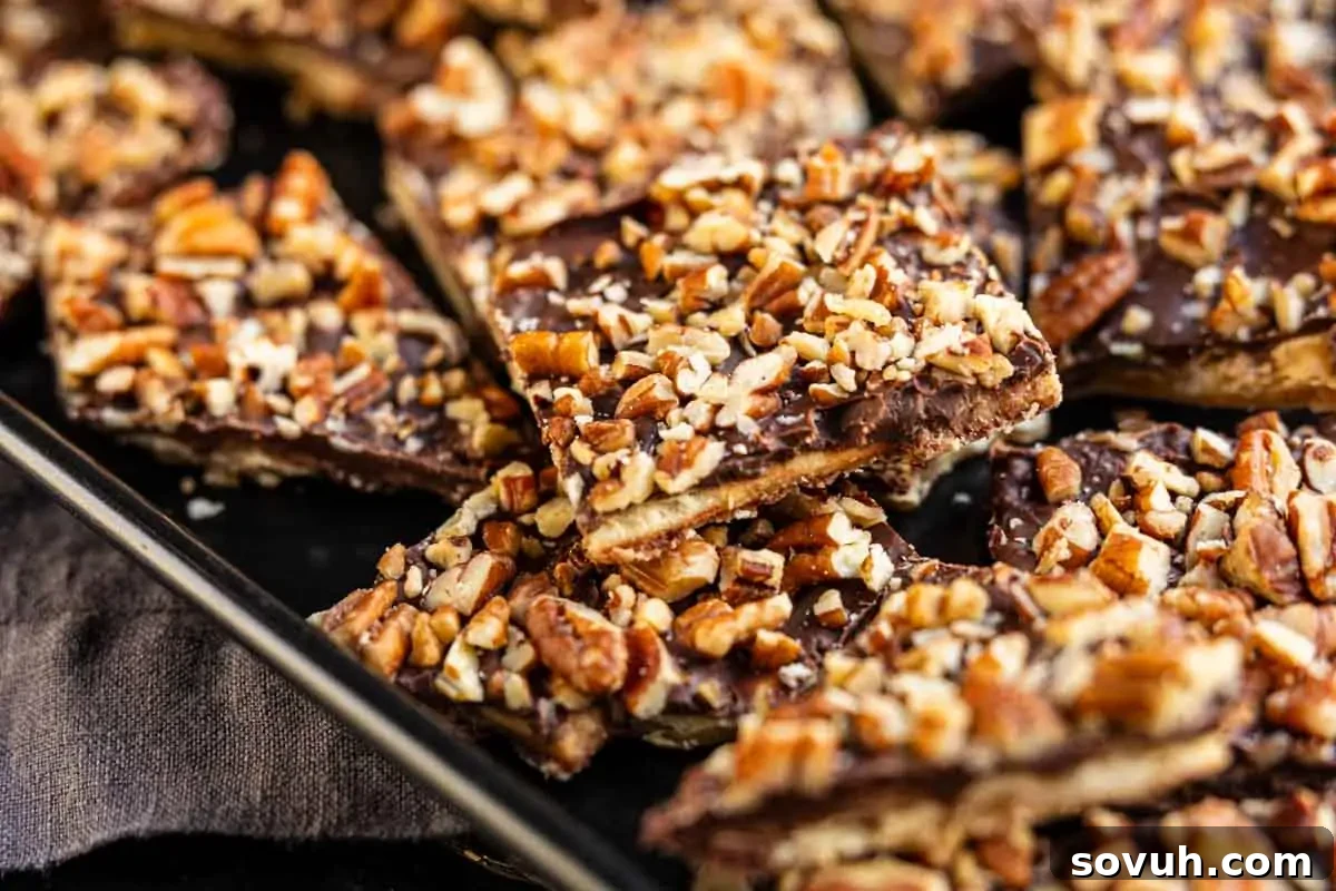 A close-up of a baking sheet filled with golden-brown Saltine Cracker Toffee squares, generously topped with a rich layer of chopped nuts and melted chocolate, ready to be broken into individual treats.