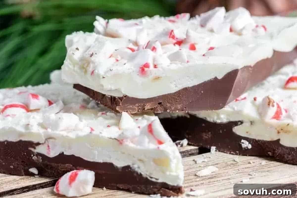 A close-up shot of refreshing peppermint bark, showcasing distinct layers of glossy dark chocolate and creamy white chocolate, generously adorned with vibrant crushed peppermint candies, all resting on a natural wooden surface.