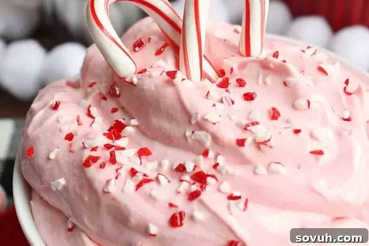 An inviting close-up of a luscious, light pink whipped dessert, elegantly topped with a generous scattering of crushed peppermint candies and two festive candy canes, ready to be enjoyed with dippers.