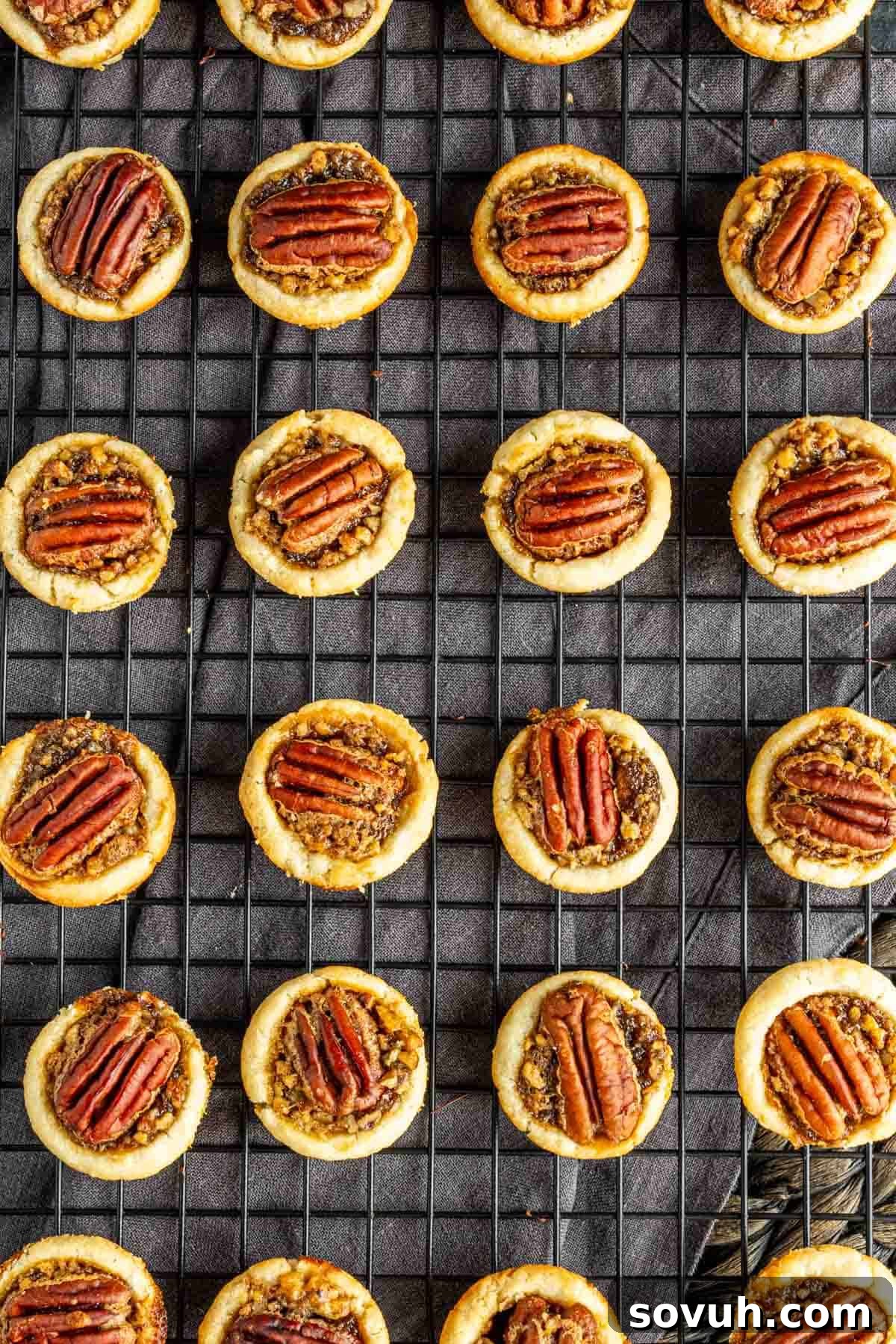 Mini pecan tarts on a cooling rack, each topped with a pecan half, arranged in neat rows.