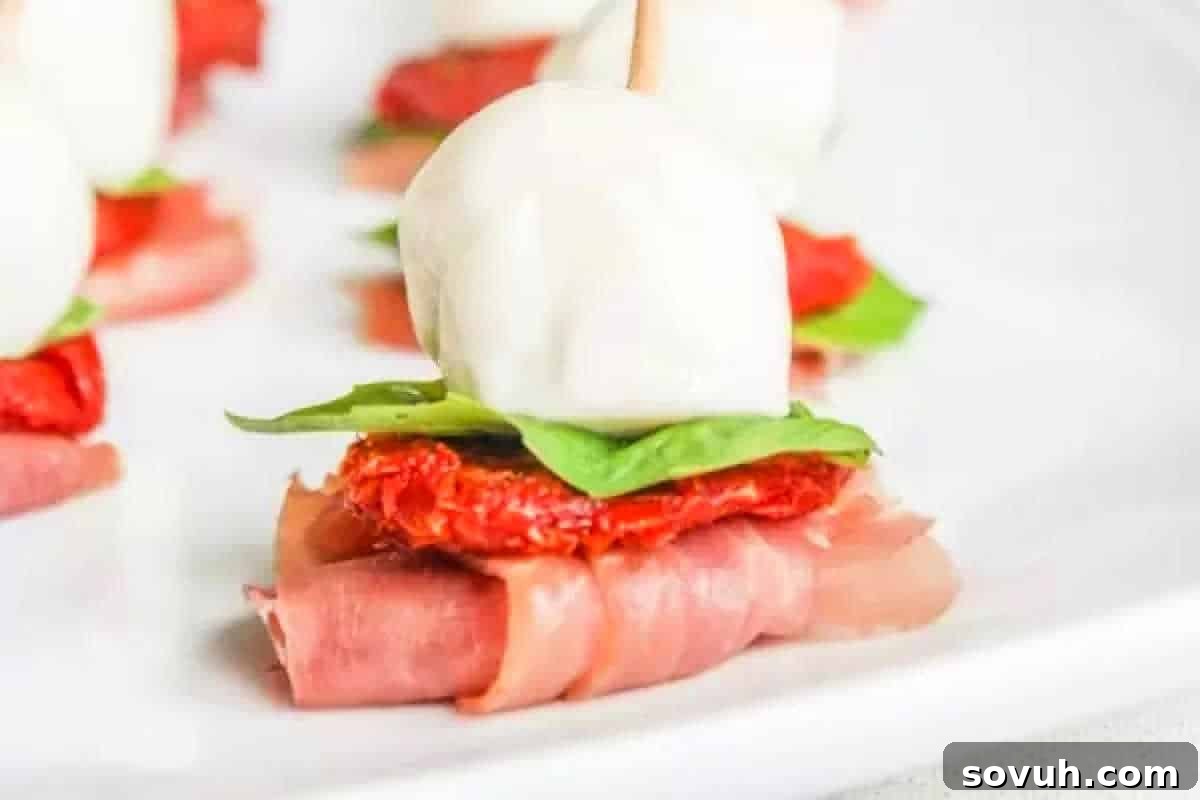 Caprese skewer with mozzarella, basil, sun-dried tomato, and prosciutto on a white plate.