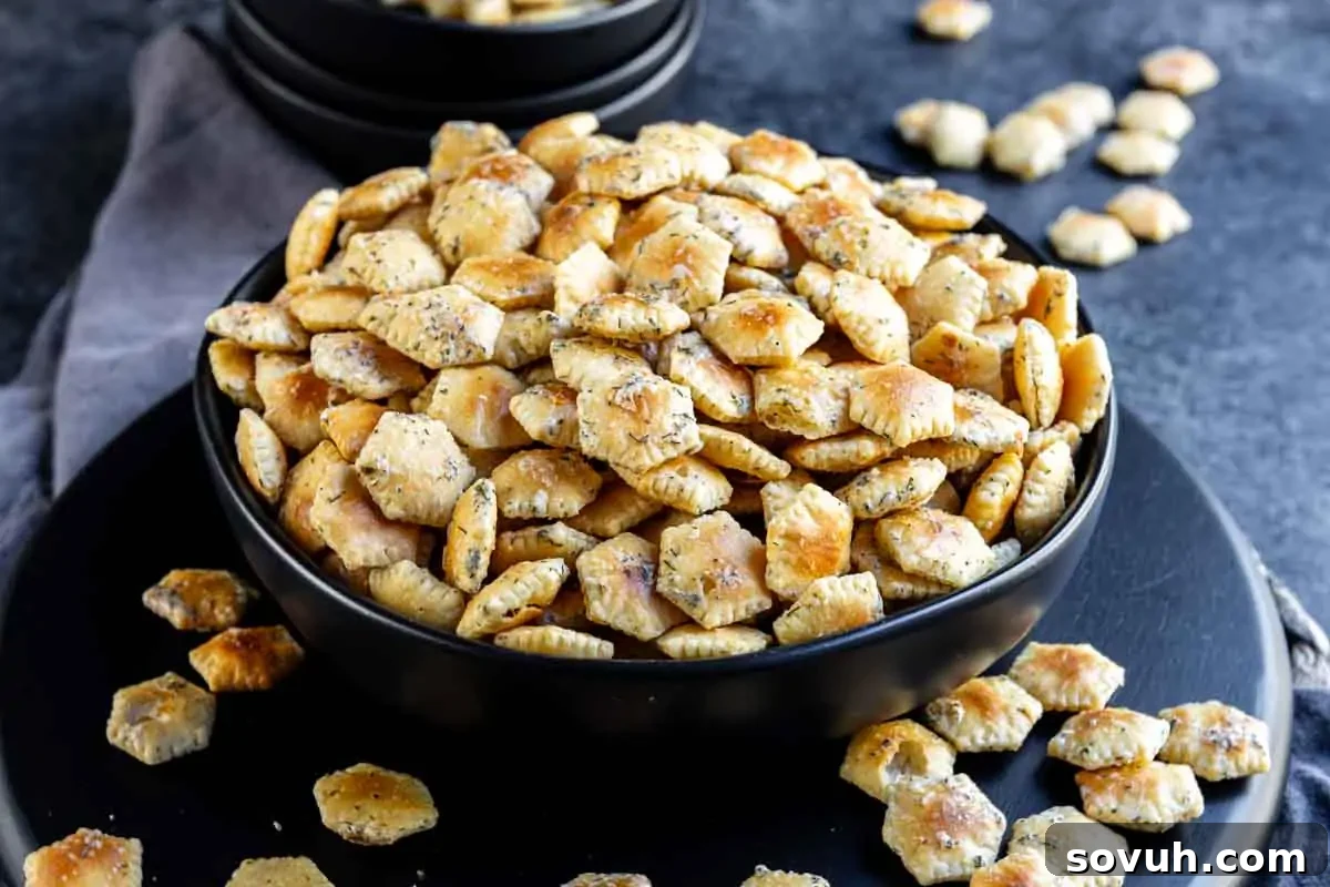 A black bowl filled with seasoned oyster crackers on a dark surface, surrounded by a few scattered crackers.
