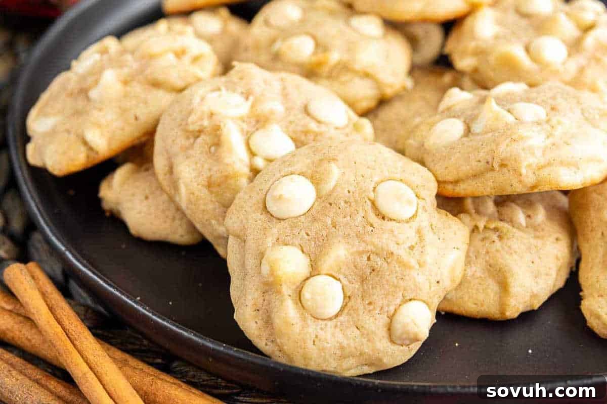 A festive plate of soft eggnog cookies with white chocolate chips, elegantly arranged beside aromatic cinnamon sticks, evoking holiday cheer.