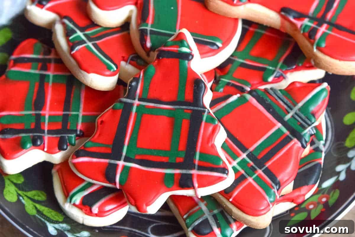 A charming plate of Christmas-themed classic sugar cookies, beautifully decorated with intricate red, green, and black plaid icing patterns.