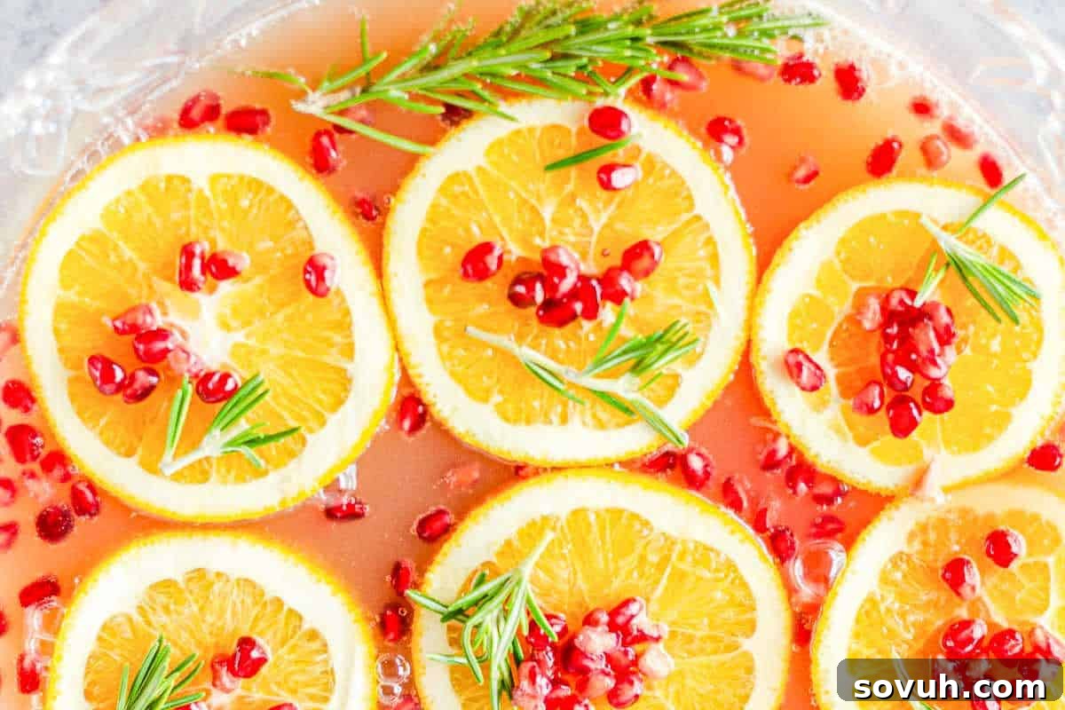 A punch bowl with orange slices, pomegranate seeds, and rosemary sprigs floating on the surface.