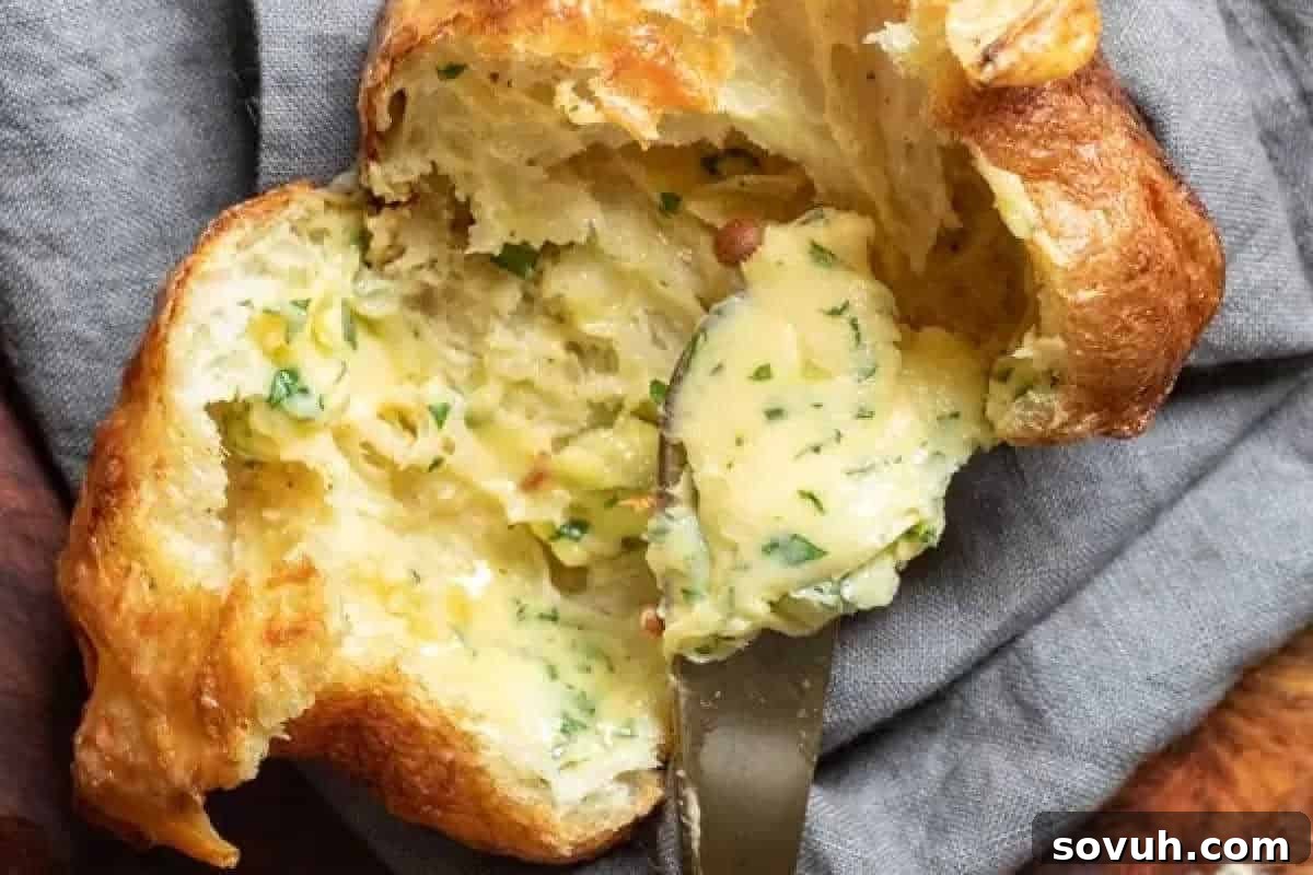 Close-up of a flaky pastry filled with creamy garlic butter and herbs, partially open with a knife placed inside.