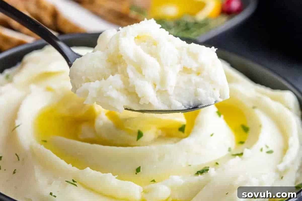A spoonful of creamy mashed potatoes with melted butter on top, garnished with herbs.