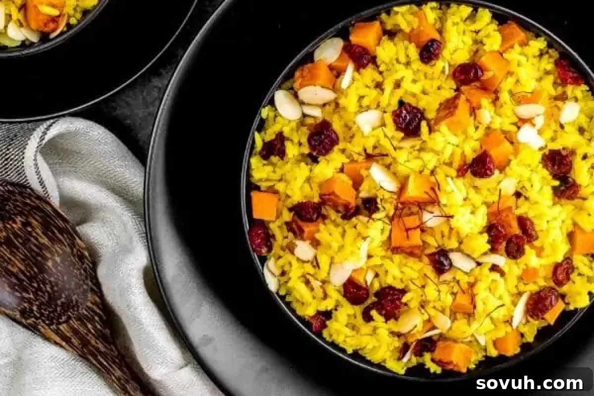 A bowl of yellow rice with diced orange pieces, nuts, and dried berries on a black plate. A wooden spoon and a cloth napkin are nearby.