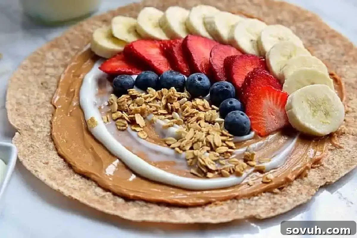 Whole wheat wrap with peanut butter, yogurt, banana slices, strawberries, blueberries, and granola on a marble surface.