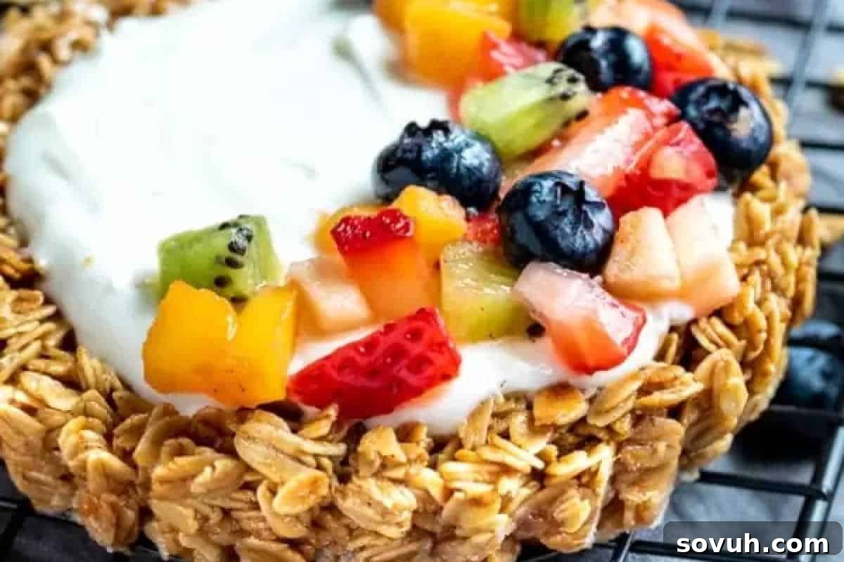 A granola tart topped with yogurt and assorted fresh fruits, including kiwi, blueberries, and strawberries, on a wire rack.